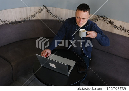 Handsome man working remotely and sipping coffee at a white table outdoors. 133702789