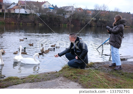 Father and teenage daughter feeding pigeons and ducks on the lake. Good family relationships. Good family values. 133702791