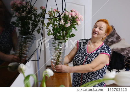 Happy smiling senior woman is enjoying planting flowers in her backyard. Gardening to create autumn floral decoration 133703813