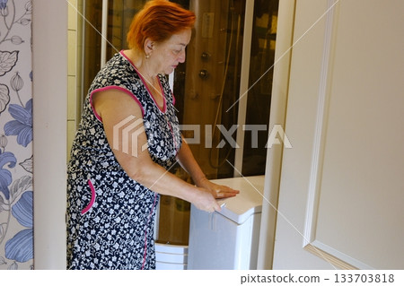 A hand reaches for the door of a modern washing machine in a laundry room. The appliance features energy efficient household technology designed for everyday use in a home setting A hand reaches for the door of a modern washing machine in a laundry room. The appliance features energy efficient household technology designed for everyday use in a home setting 133703818