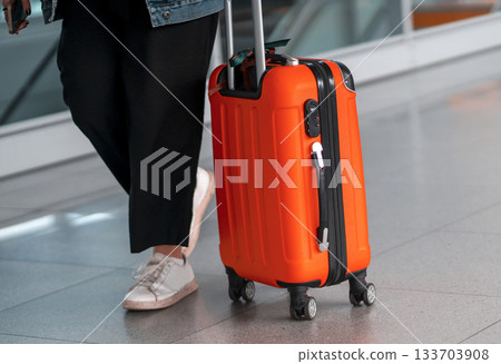 Red suitcase, a person with a travel bag at the airport. 133703908