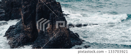 A dark rocks amist stromy wavy ocean in a cloudy weather. A dark rocks amist stromy wavy ocean in a cloudy weather. 133703921