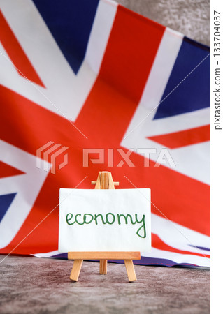 Paper note with words on ECONOMY National symbol of Great Britain. British wave the UK silky flag background. Economic growth inflation and business Paper note with words on ECONOMY National symbol of Great Britain. British wave the UK silky flag background. Economic growth inflation and business 133704037