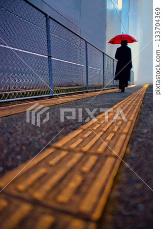 A woman with an umbrella walking on a sidewalk on a rainy day A woman with an umbrella walking on a sidewalk on a rainy day 133704369