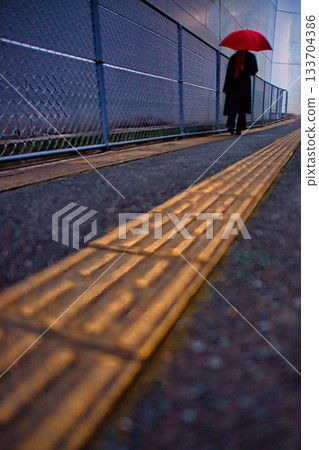 下雨天，一位女士撐著傘走在人行道上。 133704386