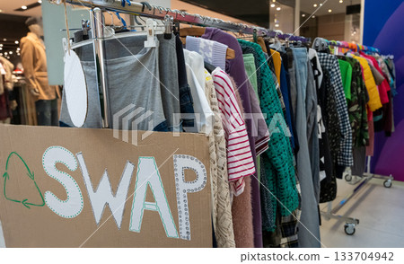 Clothes on hangers during a clothing swap event promoting sustainable fashion and reuse. Eco-friendly lifestyle, recycling, and circular economy concept encouraging people to exchange pre-loved 133704942