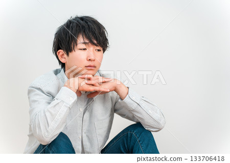 A young Asian man resting his chin on his hand and looking down blankly A young Asian man resting his chin on his hand and looking down blankly 133706418