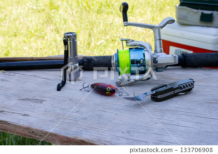 Fishing gear and camping equipment arranged on a wooden table, featuring a rod, reel, flashlight, lure, and a multi tool for outdoor leisure, hobby, and holiday activities 133706908