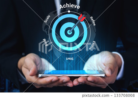 Business Professional Holding Smartphone with Digital Target Concept for Achieving Goals, Scaling Strategies, Refining Processes, and Evolving Success Gantry 133708008