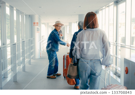 A senior couple and passengers traveling through the terminal corridor A senior couple and passengers traveling through the terminal corridor 133708843