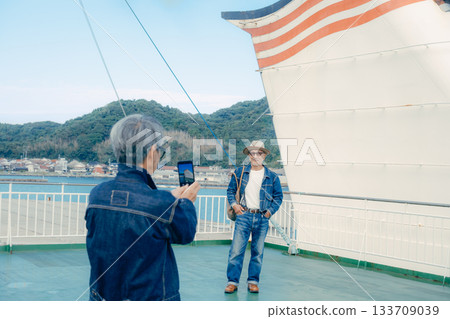 一對老年夫婦在渡輪甲板上眺望港口小鎮的旅行肖像 133709039