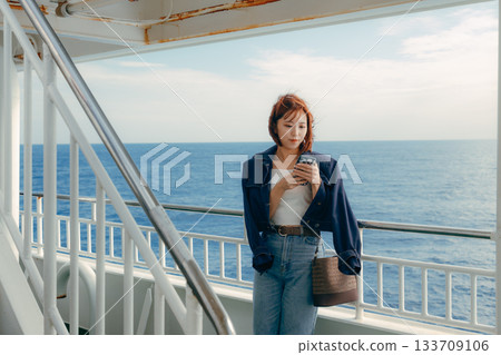 旅行場景：一位二十多歲的女子在渡輪甲板上感受海風。 133709106