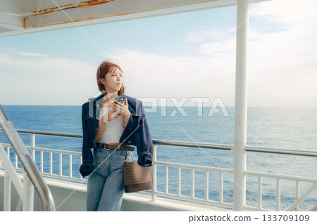 Travel scene of a woman in her twenties feeling the sea breeze on the deck of a ferry 133709109