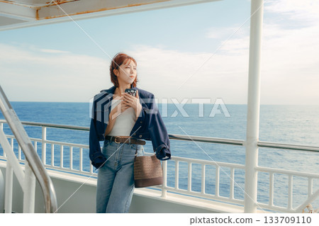 Travel scene of a woman in her twenties feeling the sea breeze on the deck of a ferry 133709110