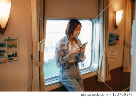 旅行場景:一位二十多歲的女子站在渡輪的窗邊。 旅行場景:一位二十多歲的女子站在渡輪的窗邊。 133709175