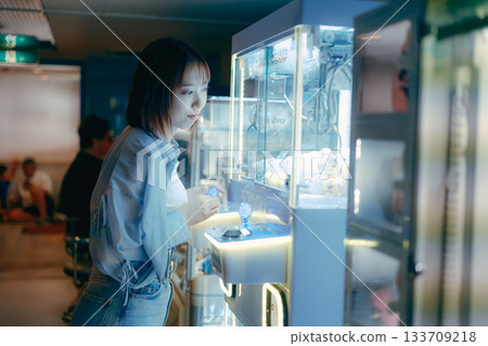 A woman in her 20s is engrossed in a crane game and looks at her boyfriend. A woman in her 20s is engrossed in a crane game and looks at her boyfriend. 133709218