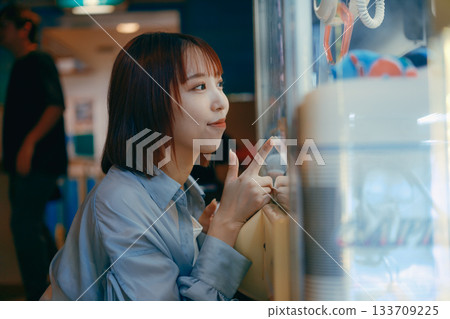 A woman in her 20s is engrossed in a crane game and looks at her boyfriend. 133709225