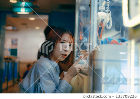 A woman in her 20s is engrossed in a crane game and looks at her boyfriend. A woman in her 20s is engrossed in a crane game and looks at her boyfriend. 133709226