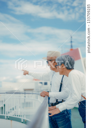 旅行場景:一對老年夫婦指著船甲板上的風景。 旅行場景:一對老年夫婦指著船甲板上的風景。 133709285