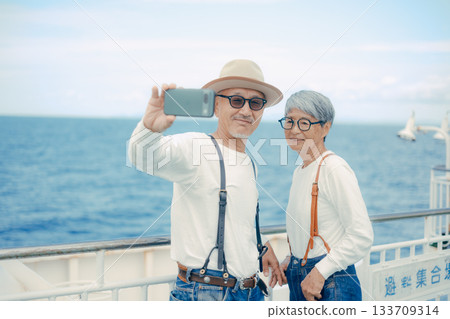 Travel scene of a senior couple taking a selfie on the deck of a ship Travel scene of a senior couple taking a selfie on the deck of a ship 133709314