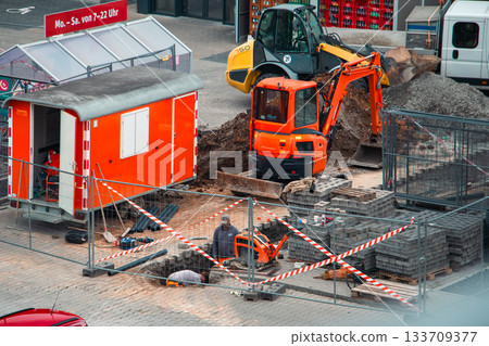 Urban Construction Site with Excavator, Worker, and Safety Barriers Urban Construction Site with Excavator, Worker, and Safety Barriers 133709377