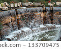 Multi-tiered stone waterfall with plants and flowers 133709475