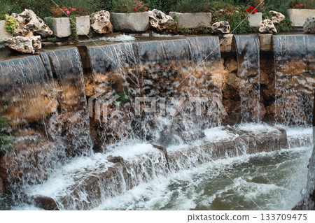 Multi-tiered stone waterfall with plants and flowers Multi-tiered stone waterfall with plants and flowers 133709475