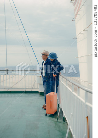 一對老年夫婦帶著行李箱，在渡輪甲板上享受旅程。 133709492