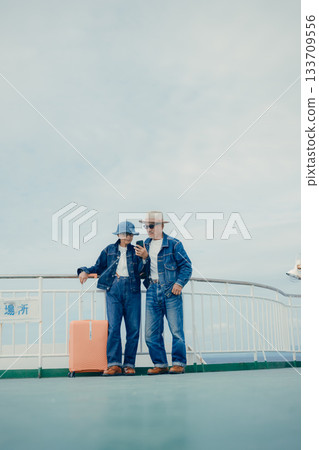 Senior couple with suitcases looking at a smartphone and pamphlet on the ferry deck Senior couple with suitcases looking at a smartphone and pamphlet on the ferry deck 133709556