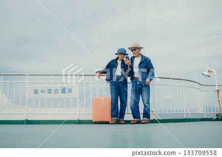 Senior couple with suitcases looking at a smartphone and pamphlet on the ferry deck Senior couple with suitcases looking at a smartphone and pamphlet on the ferry deck 133709558