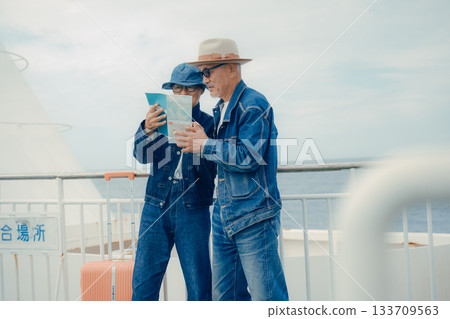 Senior couple with suitcases looking at a smartphone and pamphlet on the ferry deck Senior couple with suitcases looking at a smartphone and pamphlet on the ferry deck 133709563