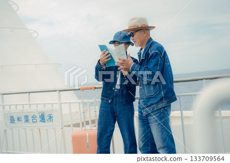 Senior couple with suitcases looking at a smartphone and pamphlet on the ferry deck Senior couple with suitcases looking at a smartphone and pamphlet on the ferry deck 133709564