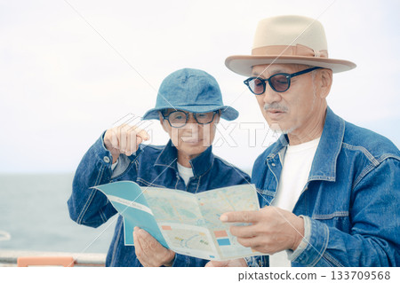 Senior couple with suitcases looking at a smartphone and pamphlet on the ferry deck Senior couple with suitcases looking at a smartphone and pamphlet on the ferry deck 133709568