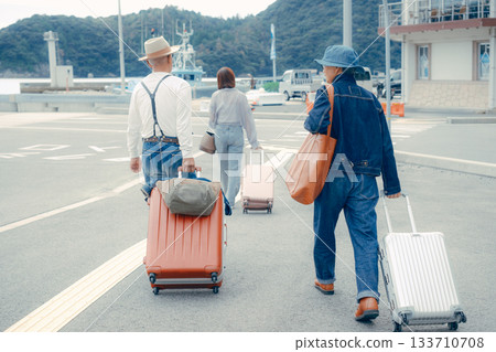 Back view of three people walking through the harbor with suitcases 133710708
