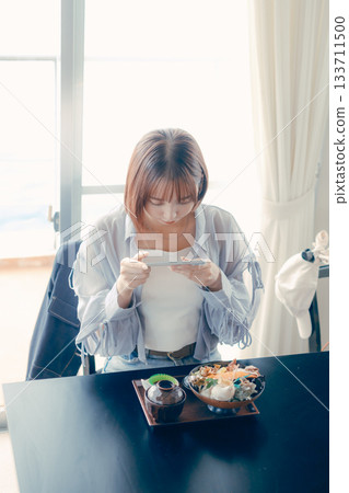 一位二十多歲的女子在海鮮碗前操作智慧型手機。 133711500