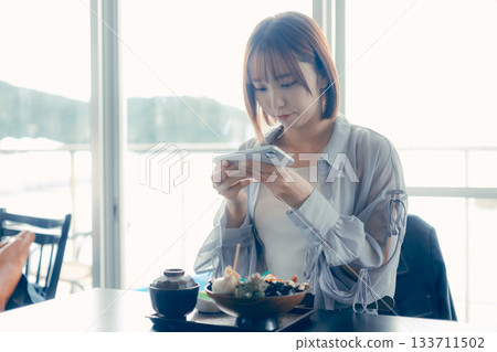 A woman in her twenties operating a smartphone in front of a seafood bowl A woman in her twenties operating a smartphone in front of a seafood bowl 133711502