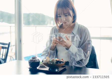 一位二十多歲的女子在海鮮碗前操作智慧型手機。 133711505
