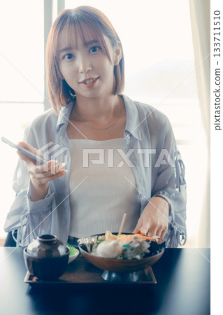 一位二十多歲的女子在海鮮碗前操作智慧型手機。 133711510