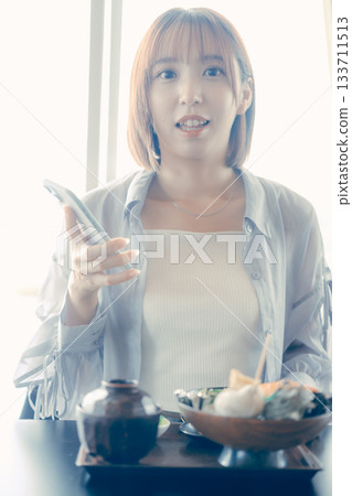 A woman in her twenties operating a smartphone in front of a seafood bowl A woman in her twenties operating a smartphone in front of a seafood bowl 133711513