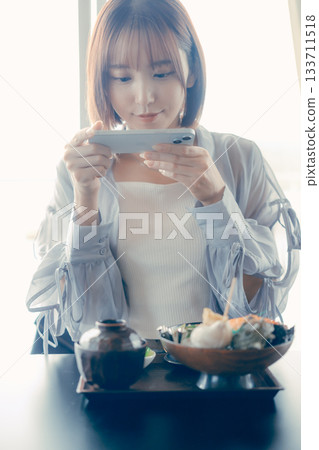 一位二十多歲的女子在海鮮碗前操作智慧型手機。 133711518
