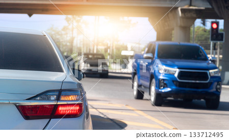 Rear side of white car with trun on right signal. Car is parked at an intersection. A car from the opposite direction drives past the intersection under the overpass. With blurred traffic red control. Rear side of white car with trun on right signal. Car is parked at an intersection. A car from the opposite direction drives past the intersection under the overpass. With blurred traffic red control. 133712495