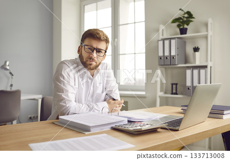 Businessman sitting at computer and filling report in office 133713008