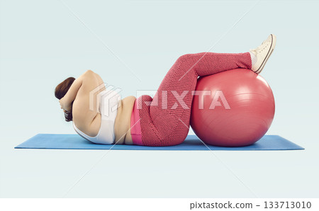 Overweight woman lying on sports mat and doing crunches exercise with Swiss ball 133713010