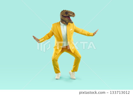 Funny showman in yellow suit and rubber dinosaur mask dancing on turquoise background. 133713012