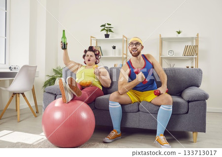 Fun young couple in sportswear watching football sports games sitting on sofa at home together. 133713017