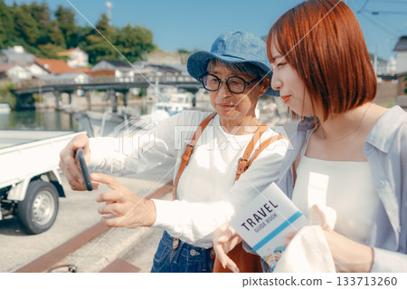 旅途中,一位六十多歲的老人和一位二十多歲的女子正在看智慧型手機。 旅途中,一位六十多歲的老人和一位二十多歲的女子正在看智慧型手機。 133713260