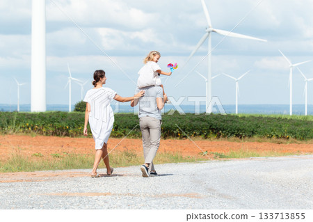 Happy cheerful caucasian white family with daughter are walking and relaxing together in the daytime in nature with windmill towers in background. Happy family activity concept. Happy cheerful caucasian white family with daughter are walking and relaxing together in the daytime in nature with windmill towers in background. Happy family activity concept. 133713855