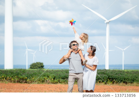 Happy cheerful caucasian white family with daughter are walking and relaxing together in the daytime in nature with windmill towers in background. Happy family activity concept. Happy cheerful caucasian white family with daughter are walking and relaxing together in the daytime in nature with windmill towers in background. Happy family activity concept. 133713856