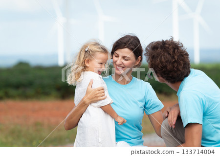 Happy cheerful caucasian white family with daughter are walking and relaxing together in the daytime in nature with windmill towers in background. Happy family activity concept. Happy cheerful caucasian white family with daughter are walking and relaxing together in the daytime in nature with windmill towers in background. Happy family activity concept. 133714004