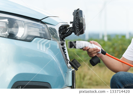 Unrecognizable Asian man holding AC type 2 EV charging connector at EV charging station, man preparing an EV - electric vehicle charging connector for recharge a vehicle. Unrecognizable Asian man holding AC type 2 EV charging connector at EV charging station, man preparing an EV - electric vehicle charging connector for recharge a vehicle. 133714420